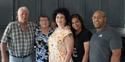 A diverse group of five adults posing together indoors, smiling warmly.