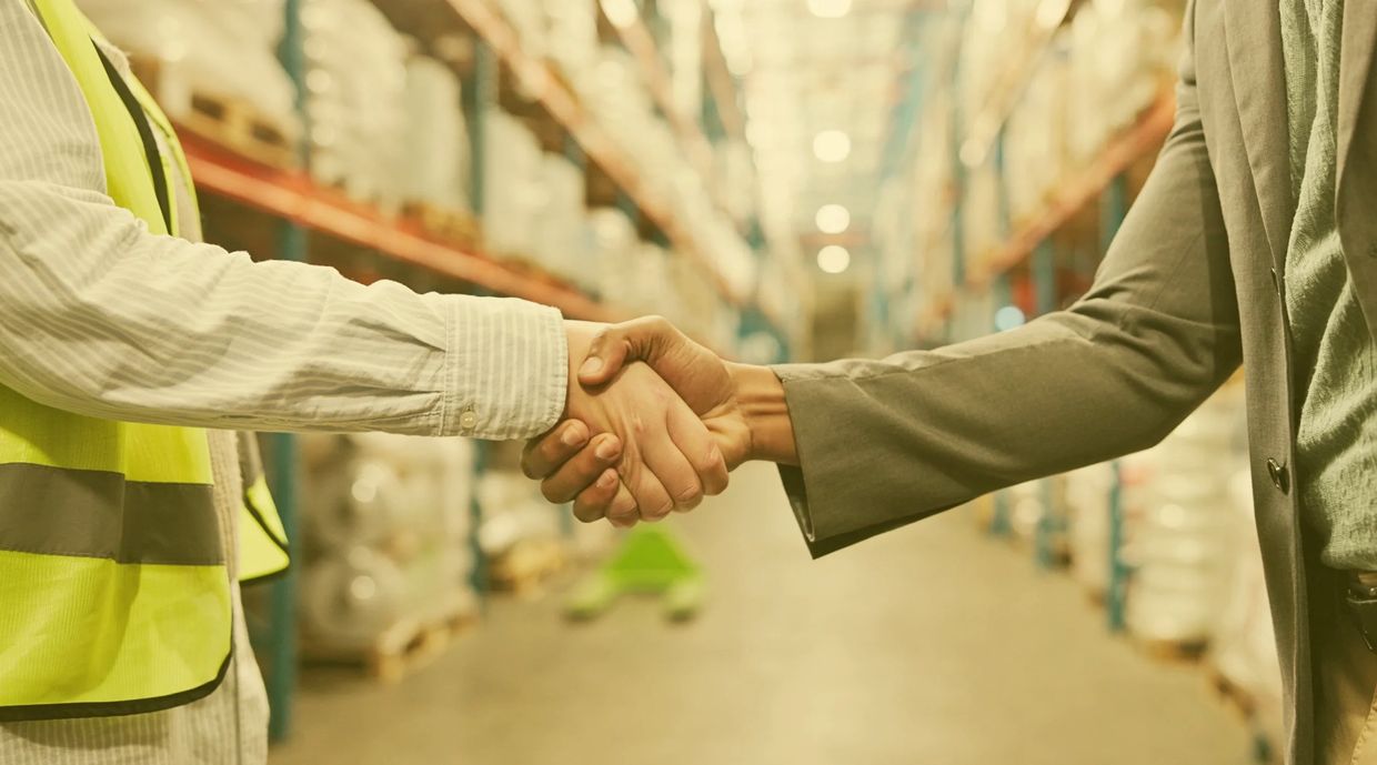 Two professionals shaking hands in a warehouse setting.