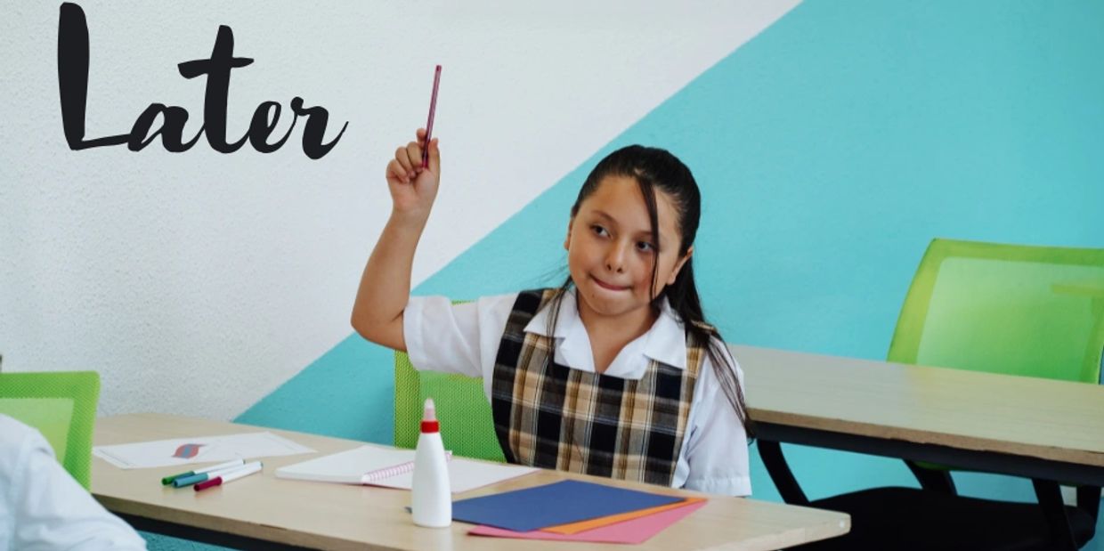 Girl in school uniform raising her hand in classroom.