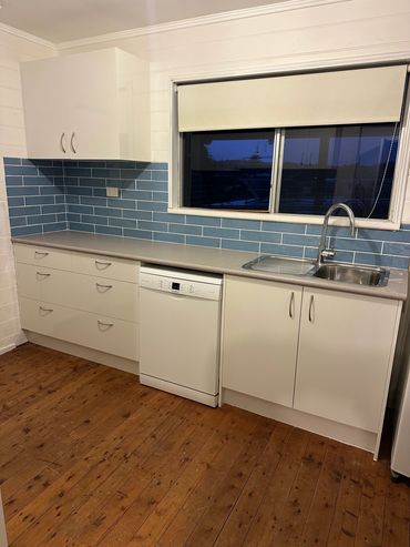 Modern kitchen with white cabinets, blue tile backsplash, and wooden floor.