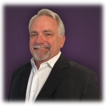 Smiling middle-aged man in a black suit and white shirt against a purple background.