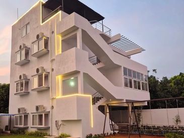 Modern three-story white building with outdoor stairs and garden swing at dusk.
