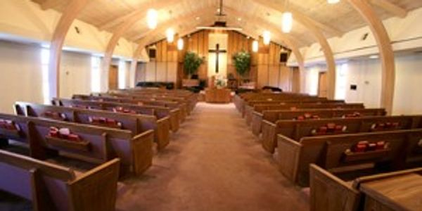 Empty Christian church sanctuary with several pews and a cross front and center.
