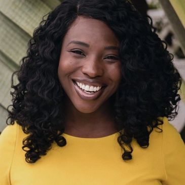 Headshot of Jannah Welcome. Black/African American female with dark, long, curly hair and big smile.