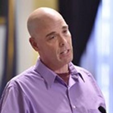 Headshot of Scott Theurer. Caucasian male, bald and wearing a purple button down.