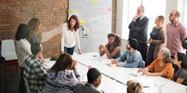 14 individuals of mixed diversity and gender standing or sitting at a table in a conference room.