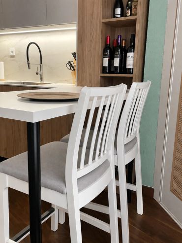 Sillas blancas con cojines grises junto a una mesa blanca en cocina moderna.