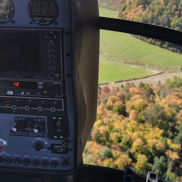 View from inside a helicopter cockpit over fall foliage and farmland.