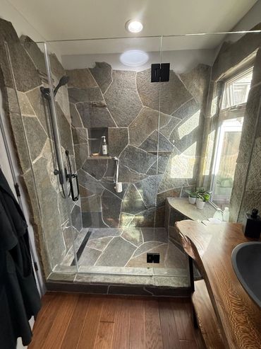 Rustic stone shower with glass enclosure and wooden floor.