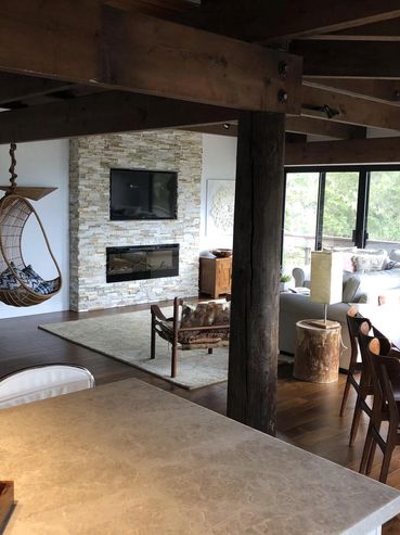 Modern living room with wooden beams, hanging chair, and stone fireplace.