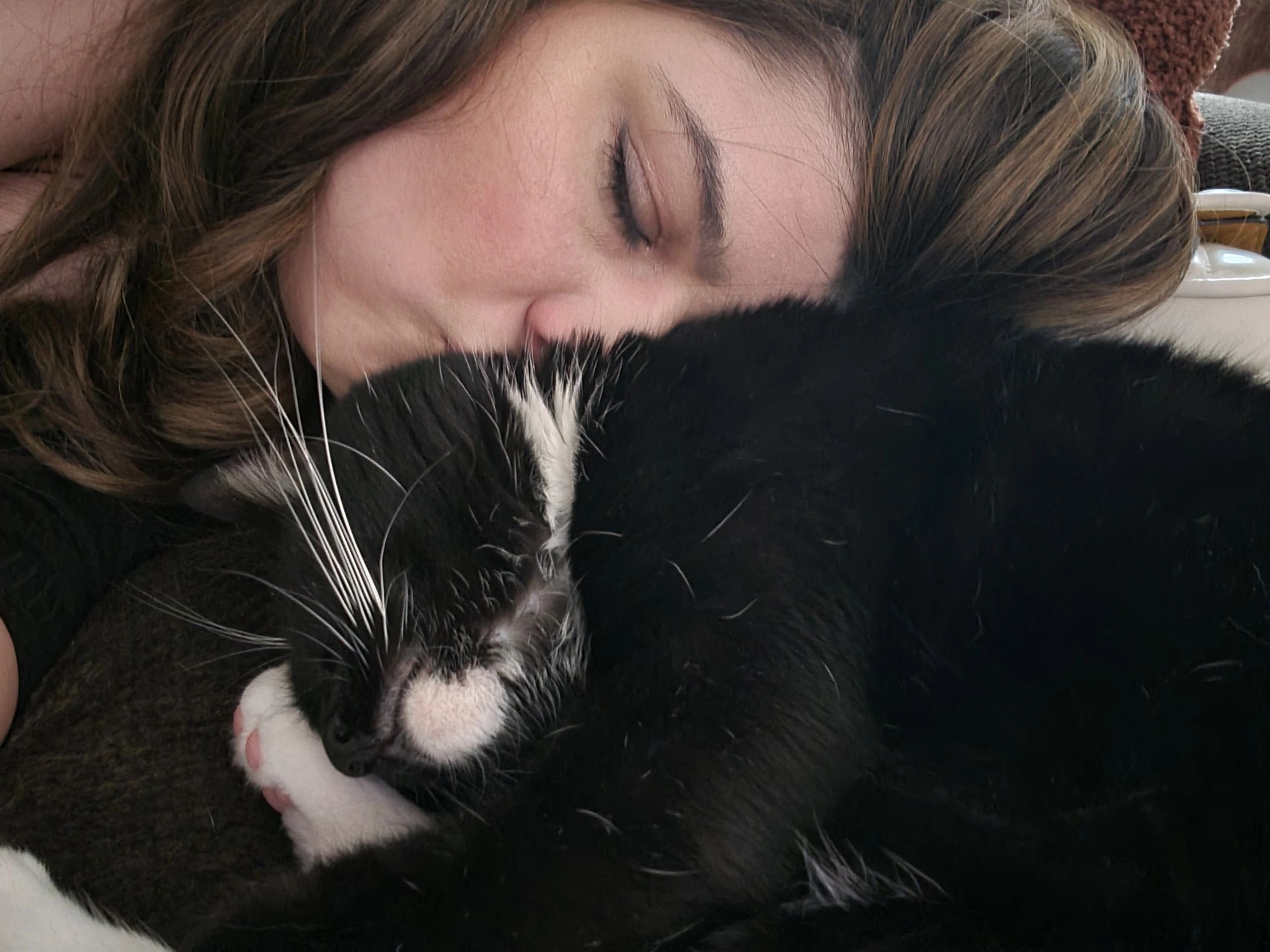 A woman snuggling a black and white cat