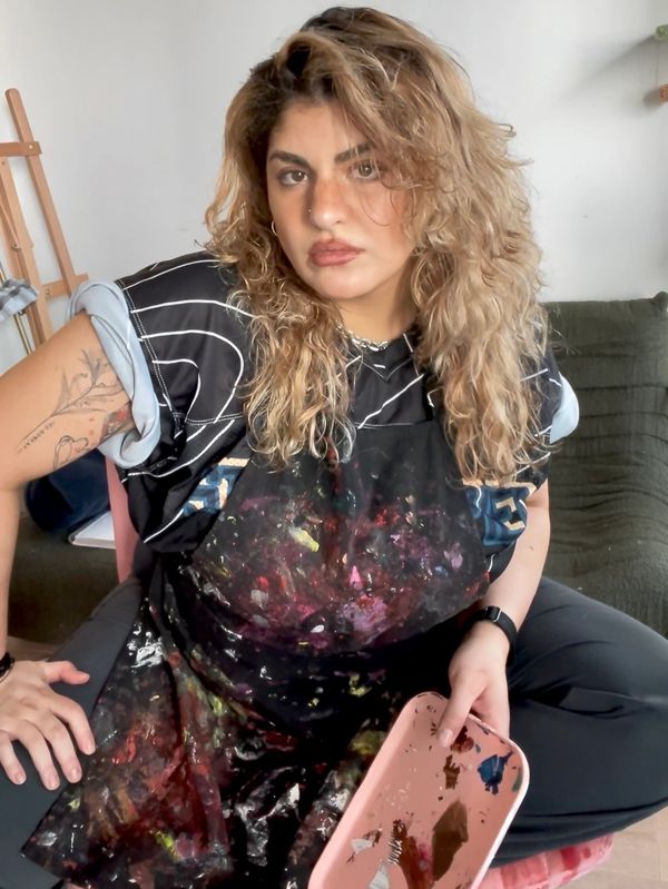 Artist with paint-splattered apron holding a palette, sitting ready to paint.