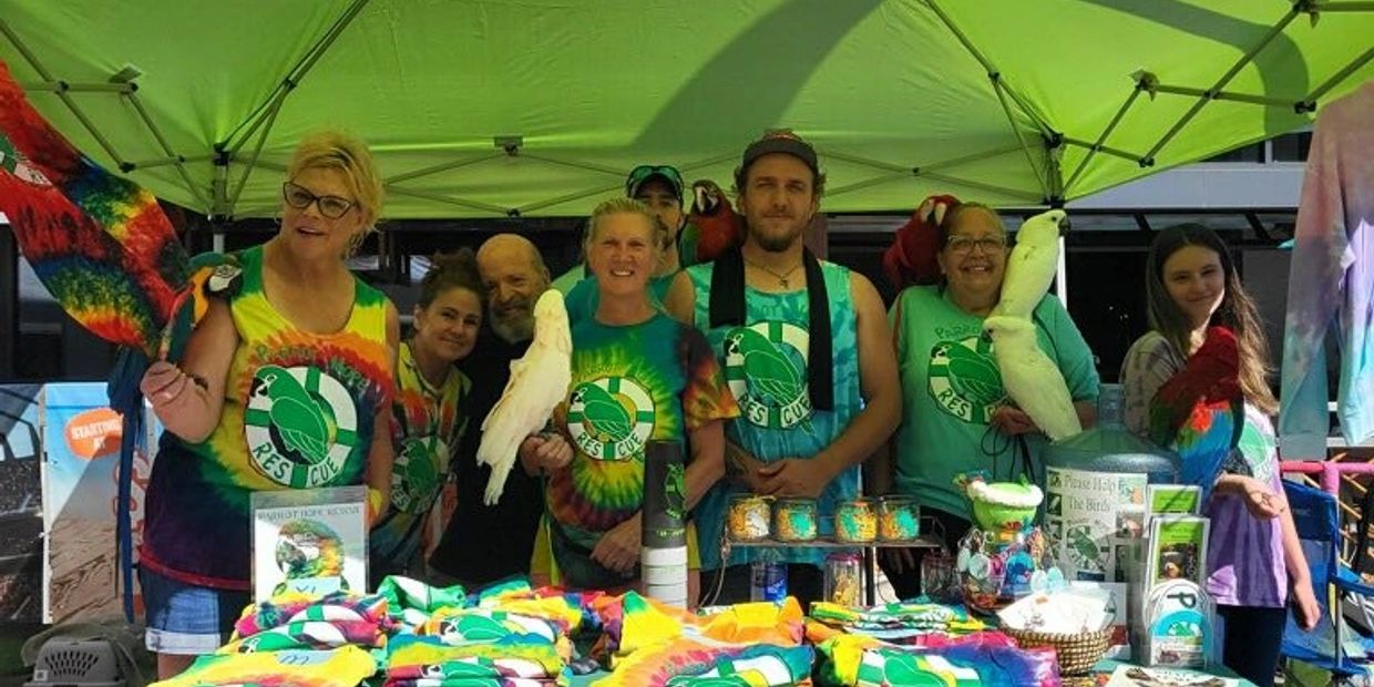 Group of people at a rescue booth with colorful shirts and parrots.