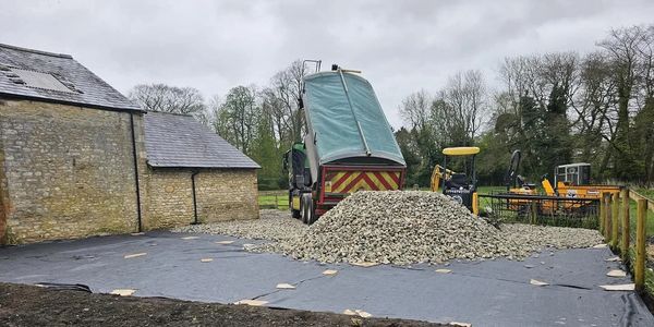 Dump truck unloading gravel near a building and machinery.