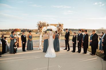 Outdoor wedding ceremony with bride, groom, and guests under a floral arch.