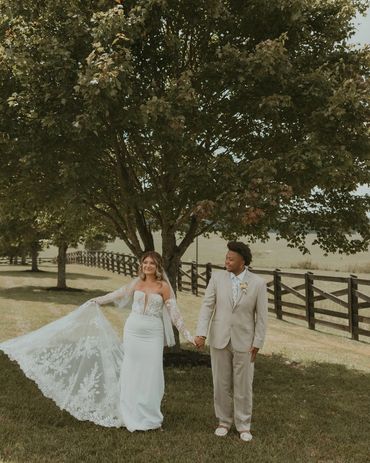 Bride and groom holding hands outdoors under a tree on their wedding day.