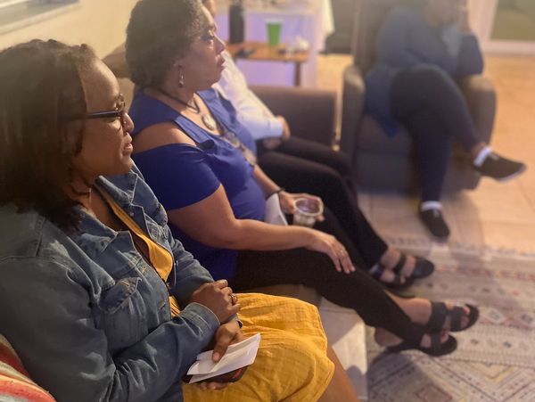 Four women seated indoors, engaged and relaxed in a cozy living room setting.