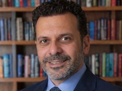 Man in suit smiling in front of a bookshelf.