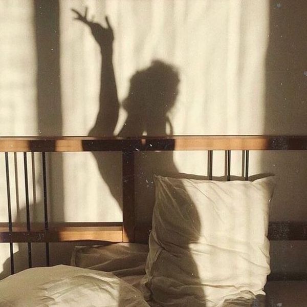 Morning light casting a soft shadow silhouette on bedroom wall — serene, earthy aesthetic