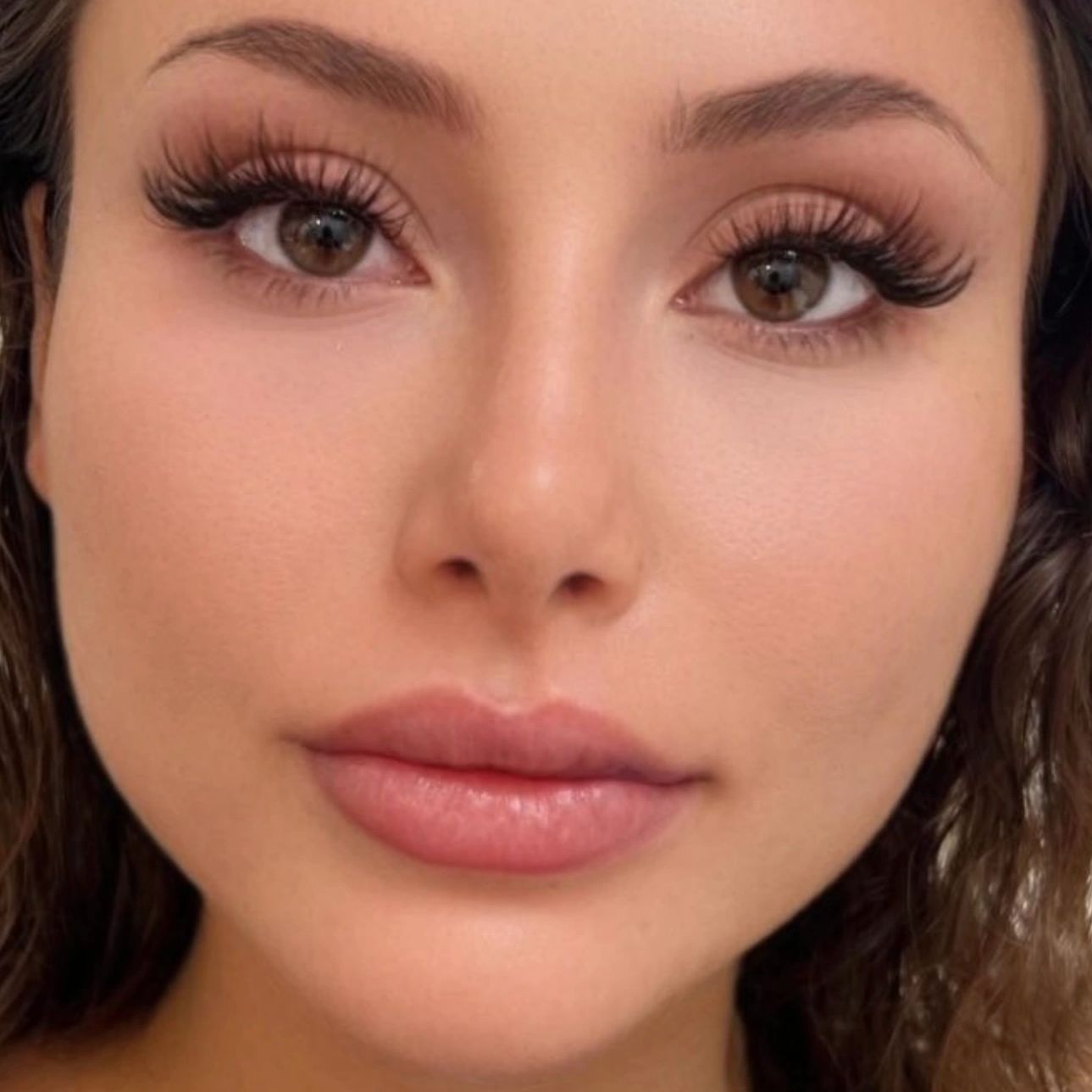 Close-up of a woman with flawless skin and long eyelashes.