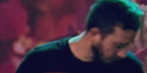 Blurry image of a man with a beard and dark hair looking down.