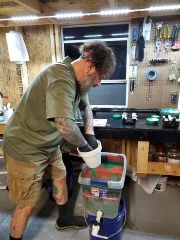 Man with tattoos working with colorful liquid in a workshop.