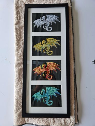 Framed embroidery of four colorful dragons in white, yellow, red, and blue.