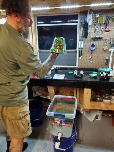 Man with tattoos holding a marbled green and red object in a workshop.