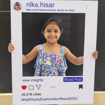 Smiling girl holding a school-themed Instagram frame celebrating exam results.