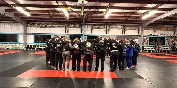 A group of martial artists standing in a circle with arms around each other.