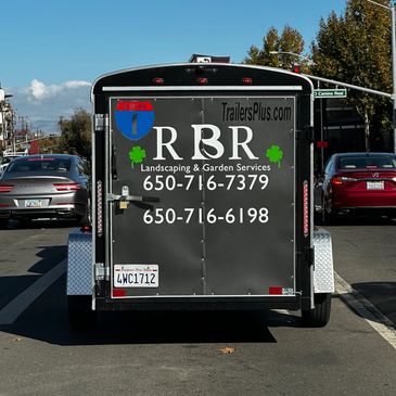 Back of a landscaping trailer with contact details on a clear day.