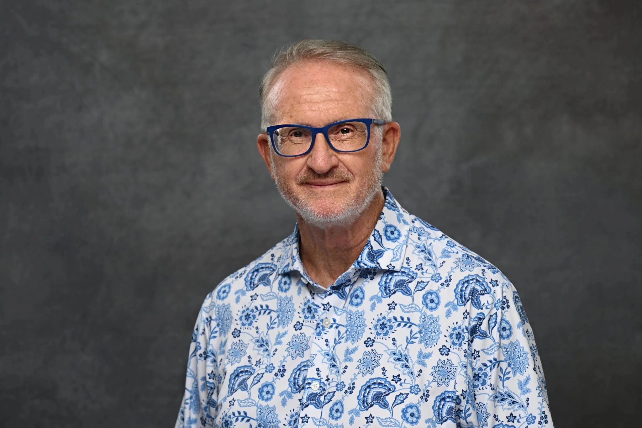 Smiling older man with blue glasses and floral shirt.