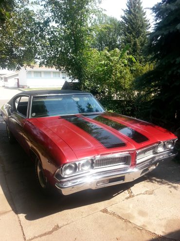 Red classic muscle car with black racing stripes parked on a driveway.