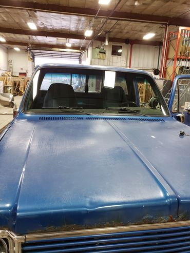 Front view of a worn blue pickup truck inside a workshop.