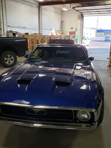 Blue classic Ford Mustang parked inside a garage with wooden crates in the background.