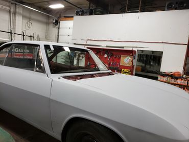 Classic car in primer paint inside a workshop with tools on the wall.