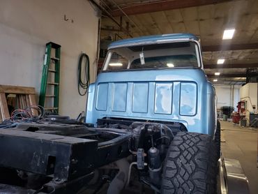 Partially restored light blue truck cab in a workshop with exposed chassis and large tires.