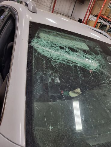 White car with severely shattered windshield inside a garage.