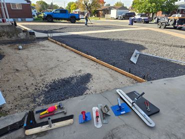 Construction tools and gravel for driveway paving with a worker in the background.