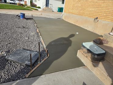 Freshly poured concrete slab next to a gravel area by a house.
