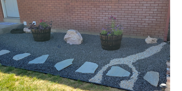 Decorative garden bed with black and white gravel, stepping stones, and flower pots.