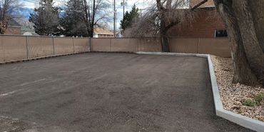 Empty fenced dirt lot with a large tree on the right side.