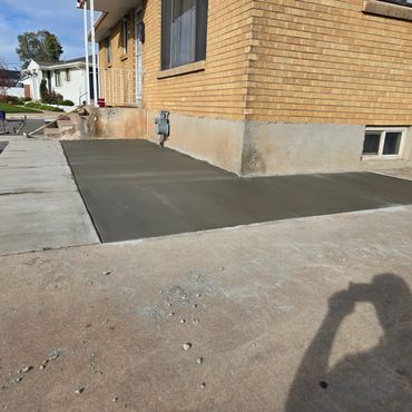 Freshly poured concrete pad beside a brick house foundation.