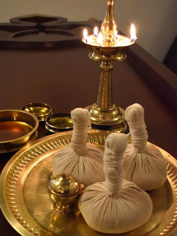 Traditional Ayurvedic massage herbs and brass oil lamp on a wooden table.