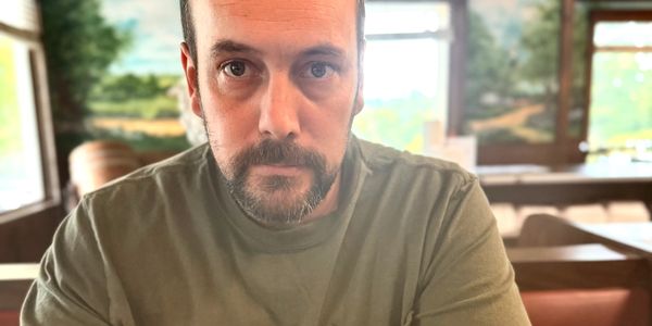 Man with a beard sitting at a diner table, looking intently at the camera.