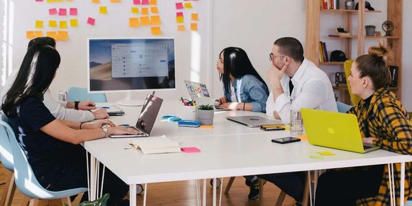 People in a meeting room with laptops and a screen.