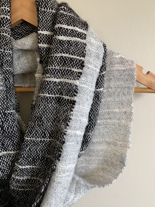 Handwoven black and white scarf hanging on a wooden hanger.
