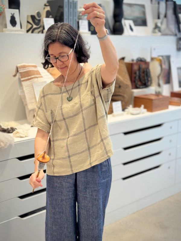 Woman spinning yarn using a drop spindle indoors.