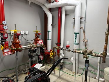 Industrial piping and valves in a utility room with labeled pipes for overflow and storm water.