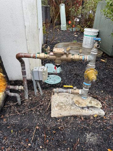 Outdoor plumbing setup with pipes and valves on a concrete slab.